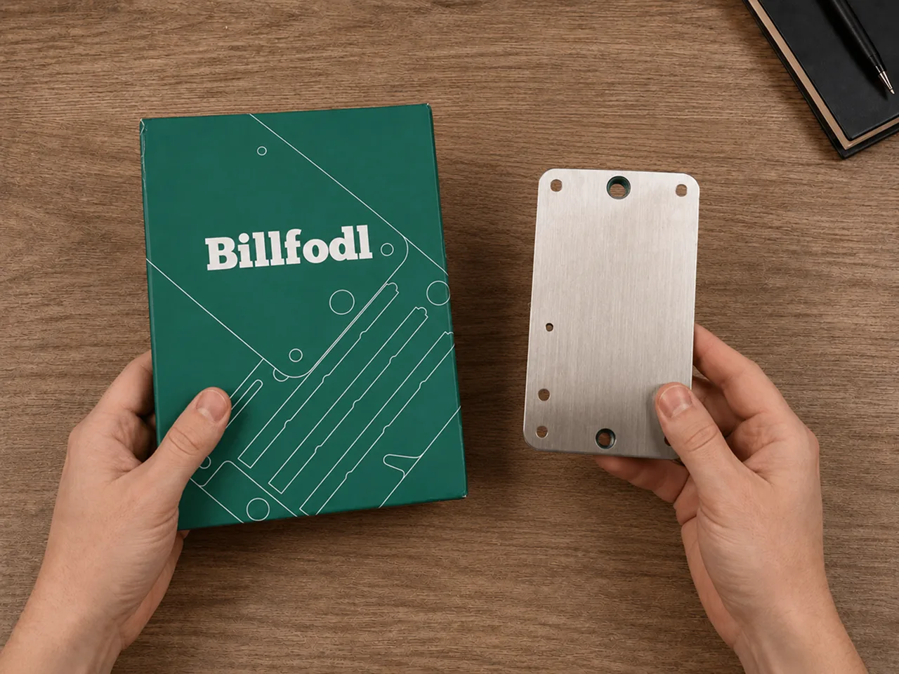 Hands presenting the Billfodl product box and closed stainless-steel tile cassette on a wooden desk