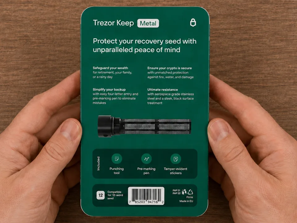 Hands holding the back of the Trezor Keep Metal box with the printed instructions and included accessories listed on the package
